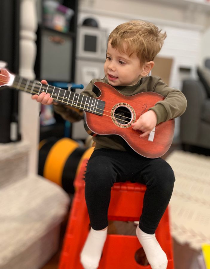 A toddler strumming a small toy guitar