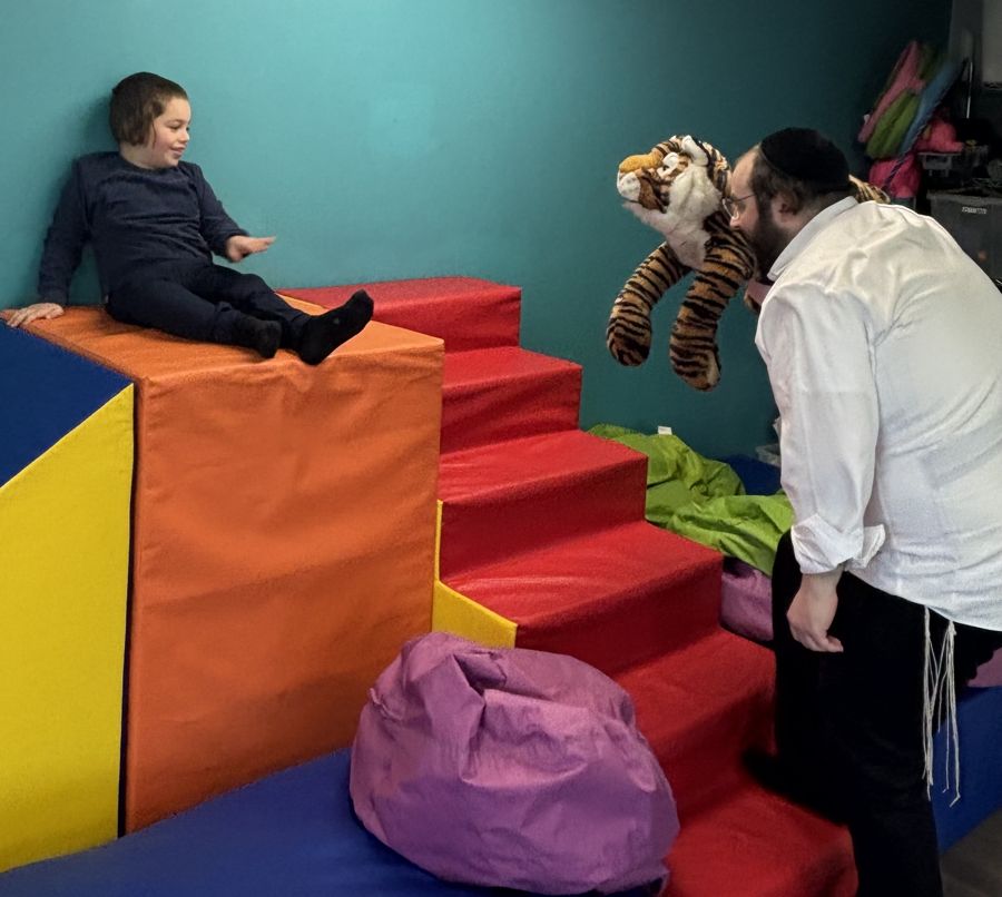 A boy on top of soft play steps smiling at a clinician holding a tiger puppet